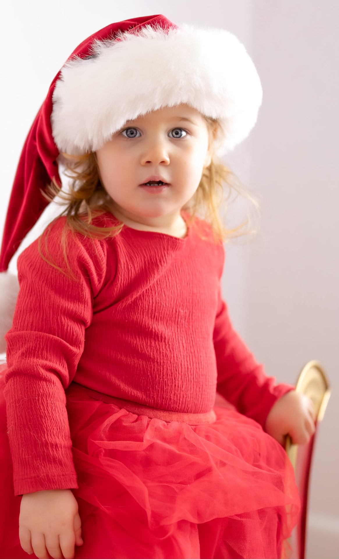 Little girl in a red dress and fluffy Santa hat sitting in a Christmas sleigh