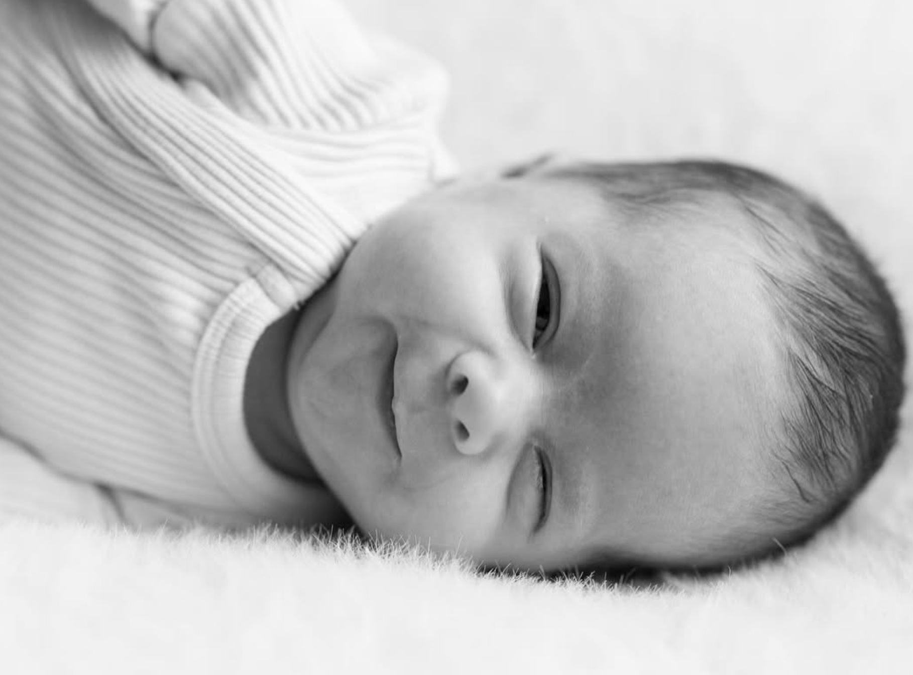 Newborn baby sleeping in a ribbed knit onesie on soft bedding, black and white